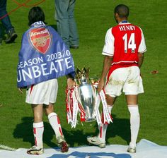 two soccer players standing on the field holding a trophy