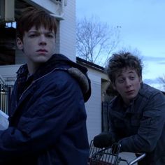 two young men standing next to each other in front of a building with an empty shopping cart