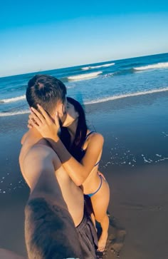 a man and woman are sitting on the beach hugging each other with their arms around one another