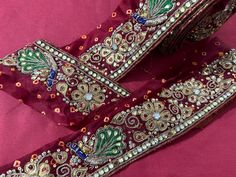 an embroidered maroon fabric with gold and green designs on the border, along with other material