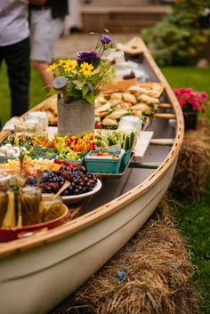 a long boat filled with lots of food on top of a grass covered field next to people