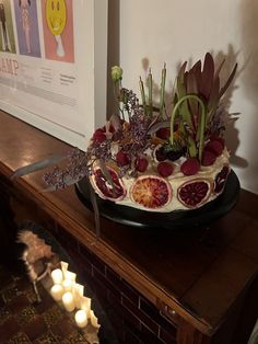 there is a cake with fruit and flowers on the table next to some candles in front of it