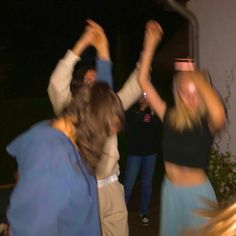 two women and one man are dancing outside at night with their arms in the air