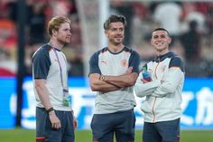 three men standing on a soccer field with their arms crossed