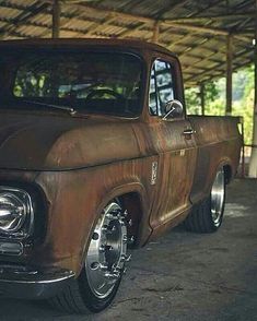 an old truck parked in a garage under a wooden roof with no one around it