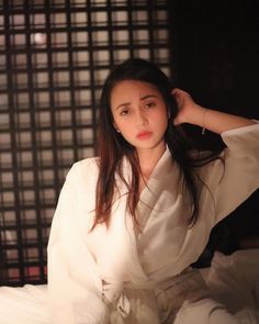 a woman sitting on top of a bed wearing a white robe