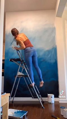 a woman standing on a ladder painting a wall