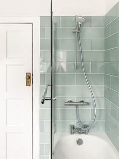 a bath tub sitting next to a white door in a bathroom with green tiles on the walls