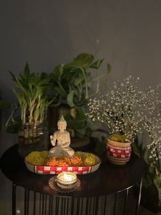 a buddha statue sitting on top of a wooden table next to potted plants and candles