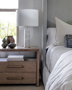 a nightstand with two vases on it next to a bed