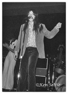 a woman singing into a microphone while standing next to a man with long hair on stage