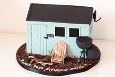 a small blue house with a lawn chair next to it on top of dirt covered ground