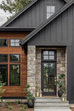 a black house with stone and wood accents on the front door, windows, and steps