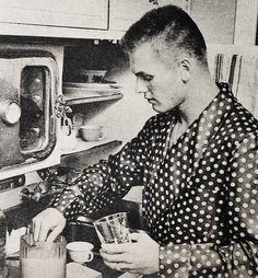 an old black and white photo of a man in the kitchen cooking something on the stove