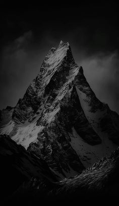 black and white photograph of the top of a snow - capped mountain with dark clouds in the background