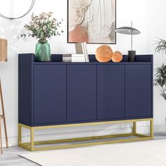 a blue sideboard with gold legs in a living room next to a painting and potted plant