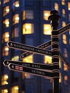 a pole with several street signs on it in front of a tall building at night