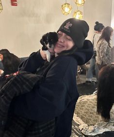 a woman holding a small black and white dog in her arms while standing next to other people