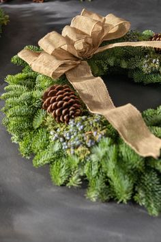 a green wreath with pine cones and evergreens on it is sitting on a table