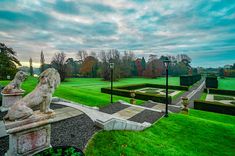 a large grassy field with statues on the grass and trees in the background at sunset