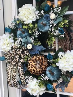 a wreath with white and blue flowers is hanging on the front door, next to a leopard print pumpkin