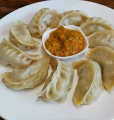 some dumplings are on a white plate with a small bowl of sauce in the middle