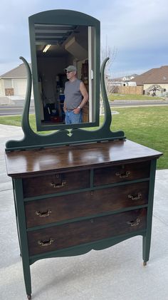 a man standing in front of a dresser with a mirror on it's side