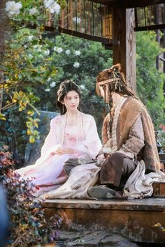 a man and woman dressed in period costumes sitting on a wooden platform next to each other