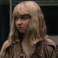 a woman with long blonde hair standing in front of a building and looking at the camera