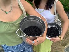 two women standing next to each other holding metal buckets filled with blackberries in their hands