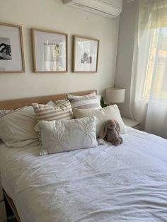 a bed with white sheets and pillows in a bedroom next to two framed pictures on the wall