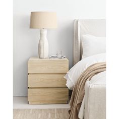 a white lamp sitting on top of a night stand next to a wooden dresser and bed