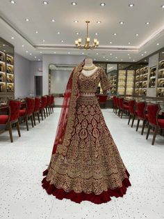 a red and gold bridal gown on display in a room filled with tables, chairs and chandeliers