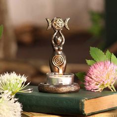 a silver statue sitting on top of a green book next to some flowers and plants