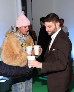 a man in a suit holding a cup and another person wearing a pink beanie