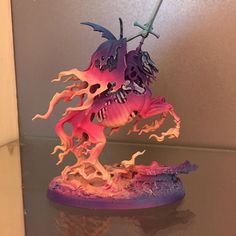 a pink and purple dragon figurine sitting on top of a glass table next to a wall