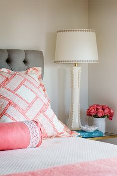 a bed with pink and white pillows on top of it next to a table lamp