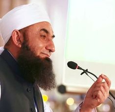 a man with a long beard speaking into a microphone while wearing a white turban