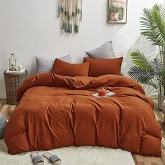 a bed with an orange comforter in a bedroom next to a potted plant