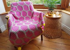 a pink and white blanket sitting on top of a chair next to a potted plant