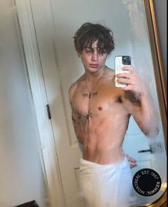 a shirtless man taking a selfie in front of a mirror with his phone