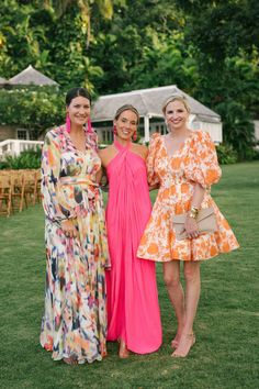 three women standing next to each other in front of some trees and chairs on the grass