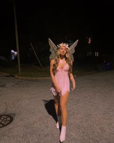 a woman in a pink fairy costume walking down the street at night with wings on her head