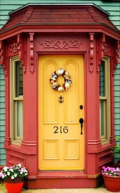 a yellow door with a wreath on it and two potted plants in front of it