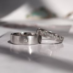 two wedding rings sitting on top of a white table next to each other with diamonds in them