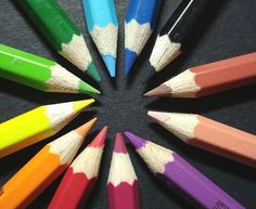 several colored pencils arranged in a circle on a black surface with the center surrounded by them