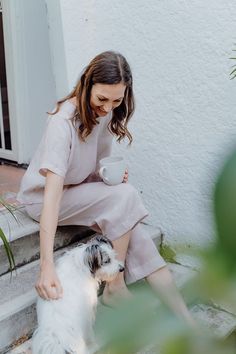 a woman is sitting on the steps with her dog and holding a coffee cup in her hand