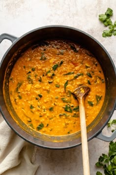 a pot filled with red lentils and garnished with parsley next to a wooden spoon