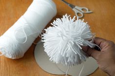 a person is holding yarn and scissors on a wooden table next to a ball of yarn