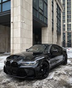 a black sports car parked in front of a tall building on a snowy day with no one around